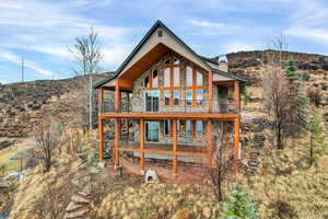 Back of property featuring stone siding, a chimney, and a balcony