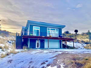 View of front of property with a wooden deck, stairs, a garage, and dirt driveway