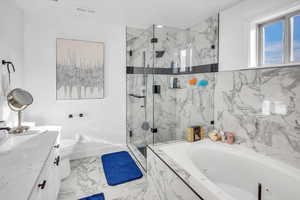 Bathroom with a whirlpool tub, a marble finish shower, vanity, and light marble finish floors