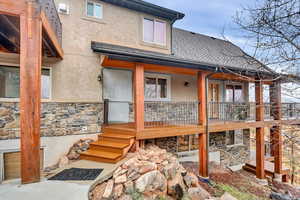 Back of property featuring stone siding, a shingled roof, stucco siding, and a deck