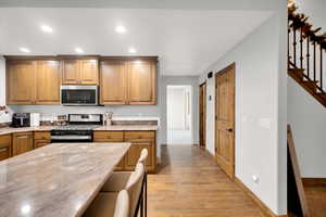 Kitchen with appliances with stainless steel finishes, recessed lighting, brown cabinets, light wood-style flooring, and a breakfast bar