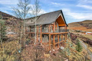 View of side of home with stone siding, a mountain view, a shingled roof, and a balcony