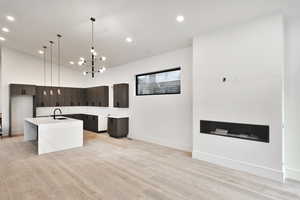 Kitchen with pendant lighting, open floor plan, light wood-style flooring, light stone countertops, waterfall island and modern cabinets