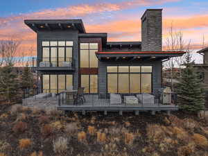 Back of house at dusk with a chimney, a balcony, and a deck