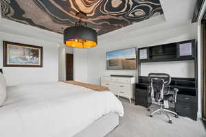 Carpeted bedroom featuring a raised ceiling and a desk