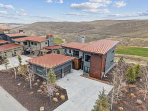 View of front of property featuring a chimney, concrete driveway, a metal roof, stone siding, and a standing seam roof
