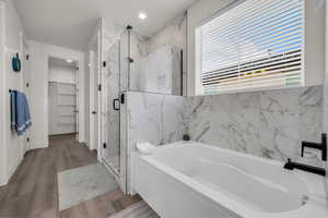 Bathroom with a garden tub, a marble finish shower, wood finished floors, a spacious closet, and recessed lighting