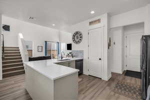 Kitchen with a peninsula, black appliances, light wood-style flooring, recessed lighting, and light stone countertops