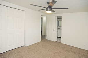 Unfurnished bedroom featuring a closet, a textured ceiling, light colored carpet, and ceiling fan