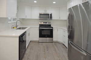 Kitchen with appliances with stainless steel finishes, light wood finished floors, light stone counters, white cabinetry, and recessed lighting