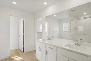 **DISCLAIMER** Interior colors & finishes may vary.Bathroom with double vanity, light wood finished floors, a stall shower, and recessed lighting