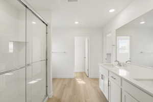 **DISCLAIMER** Interior colors & finishes may vary.Bathroom with double vanity, light wood-type flooring, a stall shower, and recessed lighting