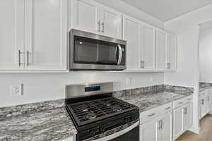 Kitchen with stainless steel appliances, white cabinetry, and light stone counters