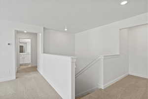 Hallway featuring an upstairs landing, light colored carpet, and recessed lighting