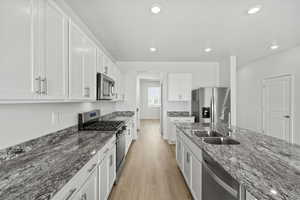 Kitchen with dark stone countertops, appliances with stainless steel finishes, white cabinets, and recessed lighting