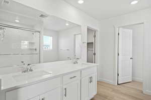 Full bathroom with light wood finished floors, double vanity, a stall shower, and recessed lighting