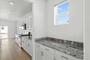 Kitchen featuring stainless steel appliances, light stone countertops, white cabinetry, recessed lighting, and light wood-type flooring
