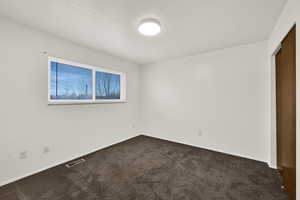 Unfurnished room featuring dark colored carpet and baseboards