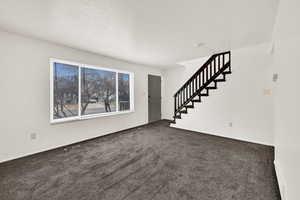 Unfurnished living room featuring stairs and dark carpet