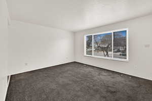 Empty room featuring dark colored carpet and a textured ceiling