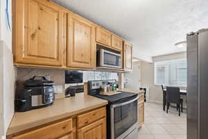 Kitchen with stainless steel appliances, light countertops, light tile patterned flooring, a textured ceiling, and backsplash