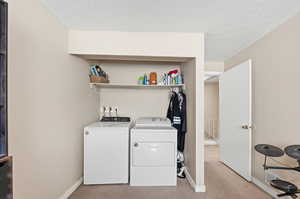 Washroom with light colored carpet, a textured ceiling, and washer and clothes dryer