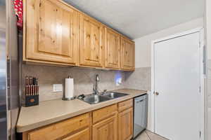 Kitchen with light countertops, dishwasher, backsplash, light brown cabinetry, and a textured ceiling