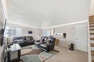Carpeted living room with a textured ceiling, plenty of natural light, and stairs
