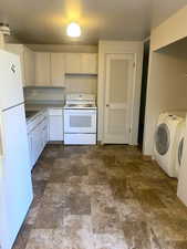 Kitchen featuring white appliances, stone finish floors, light countertops, independent washer and dryer, and white cabinetry