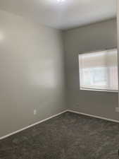Unfurnished room featuring baseboards and dark carpet