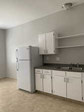 Kitchen with dark countertops, freestanding refrigerator, white cabinetry, and open shelves