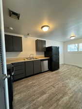 Kitchen featuring light countertops, dark cabinets, black appliances, and light wood finished floors
