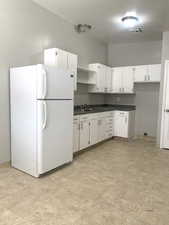Kitchen featuring dark countertops, freestanding refrigerator, open shelves, and white cabinets