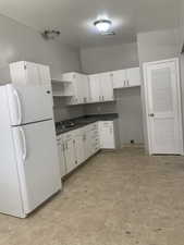 Kitchen featuring freestanding refrigerator, dark countertops, white cabinetry, and open shelves