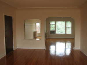 Apt # 8 > Empty room featuring wood finished floors, radiator heating unit, and arched walkways
