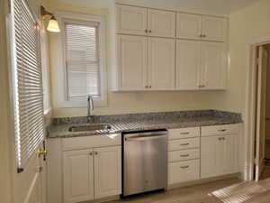 Apt # 9 > Kitchen featuring stainless steel dishwasher, white cabinetry, light stone countertops, and light wood-style flooring