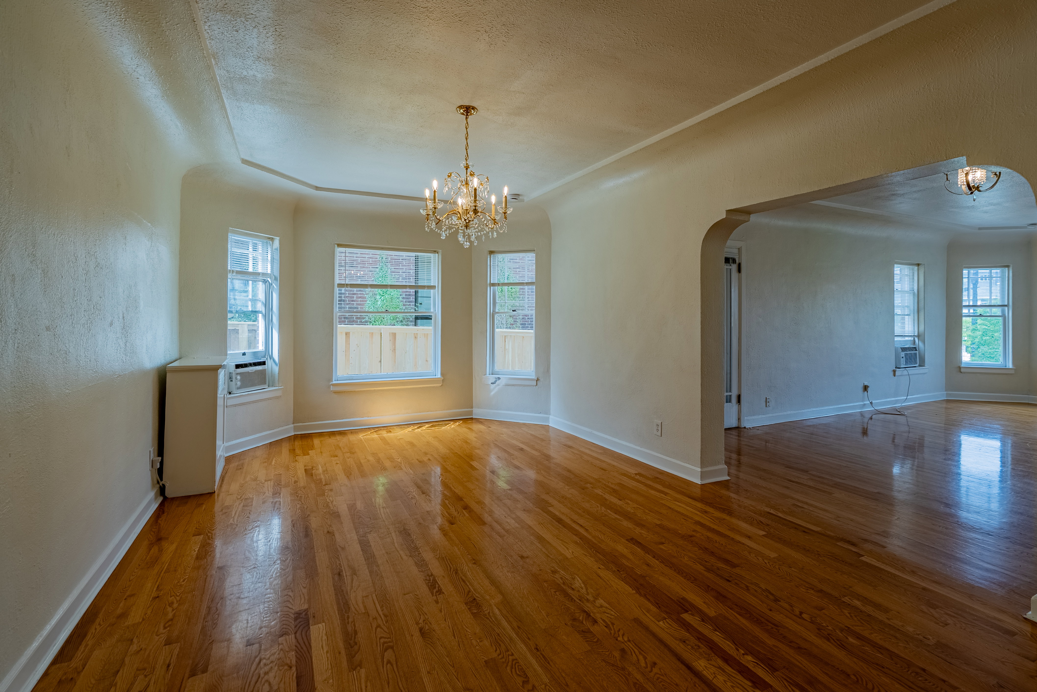 Expansive interior room featuring polished wood-finish flooring, a tiered ceiling detail, and a chandelier light fixture