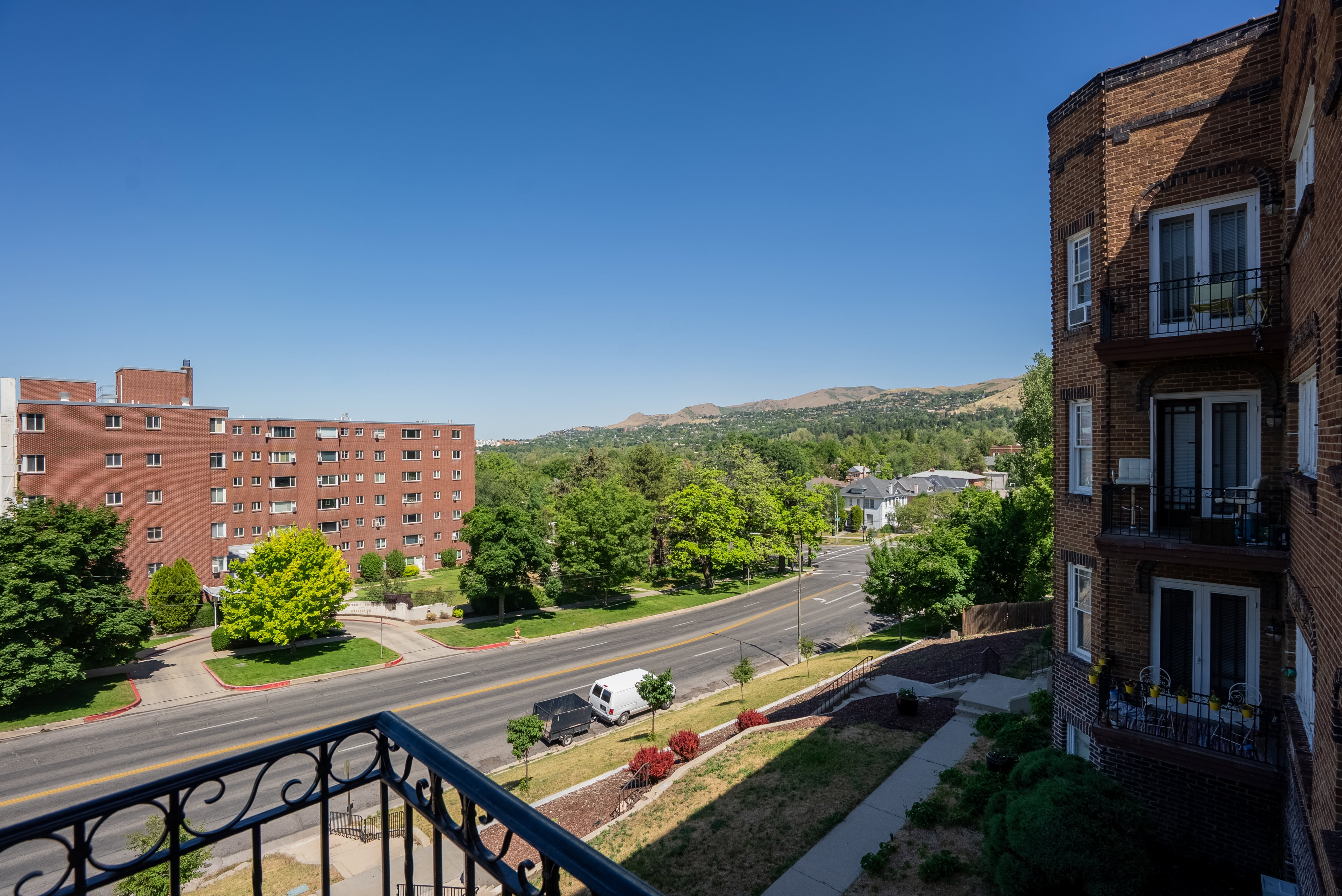 Balcony with decorative iron railing overlooking tree-lined streets, distant hills, and other residential buildings