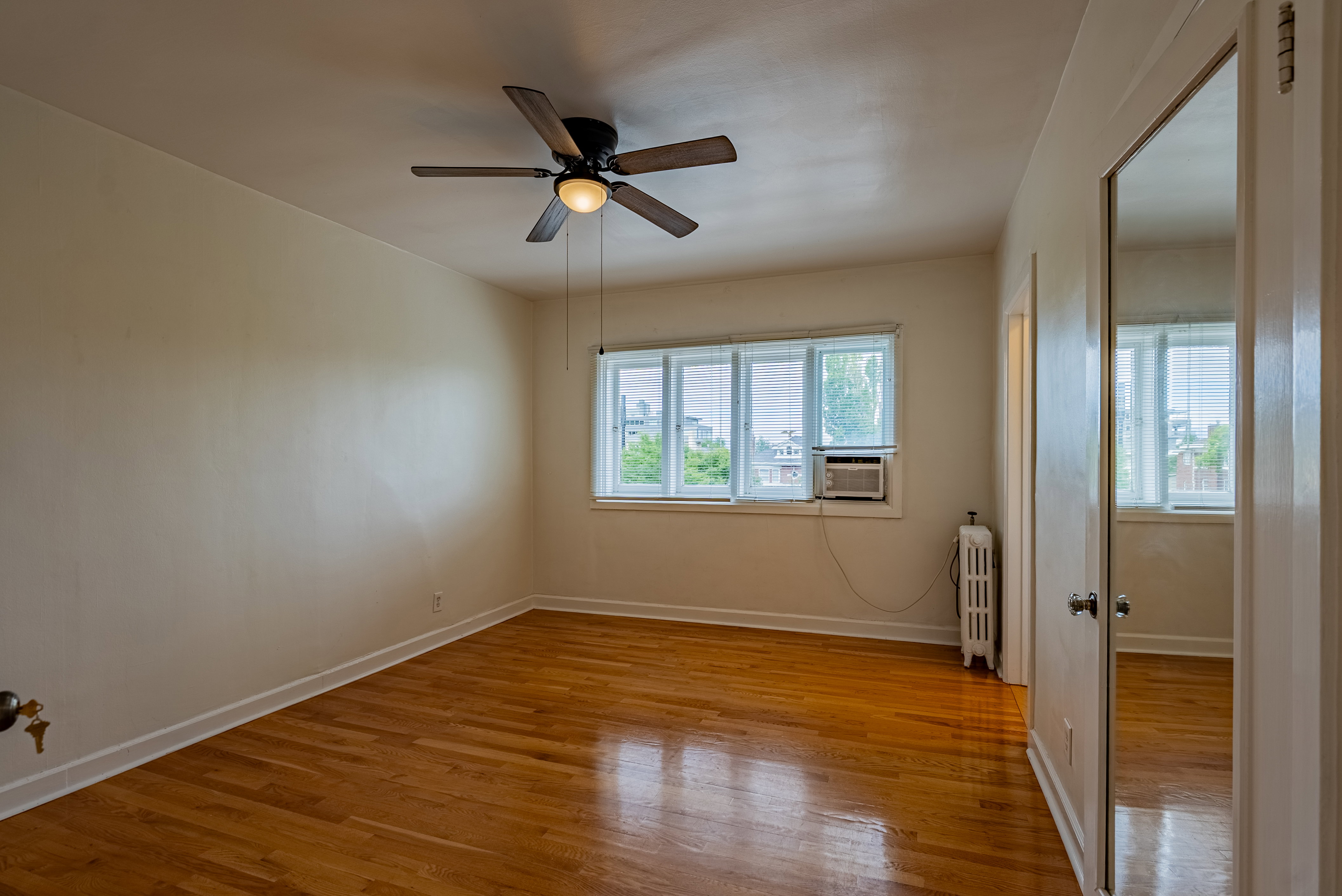 Hardwood flooring throughout featuring a ceiling fan with integrated lighting, multiple windows, a window-mounted air conditioning unit, and a mirrored closet door