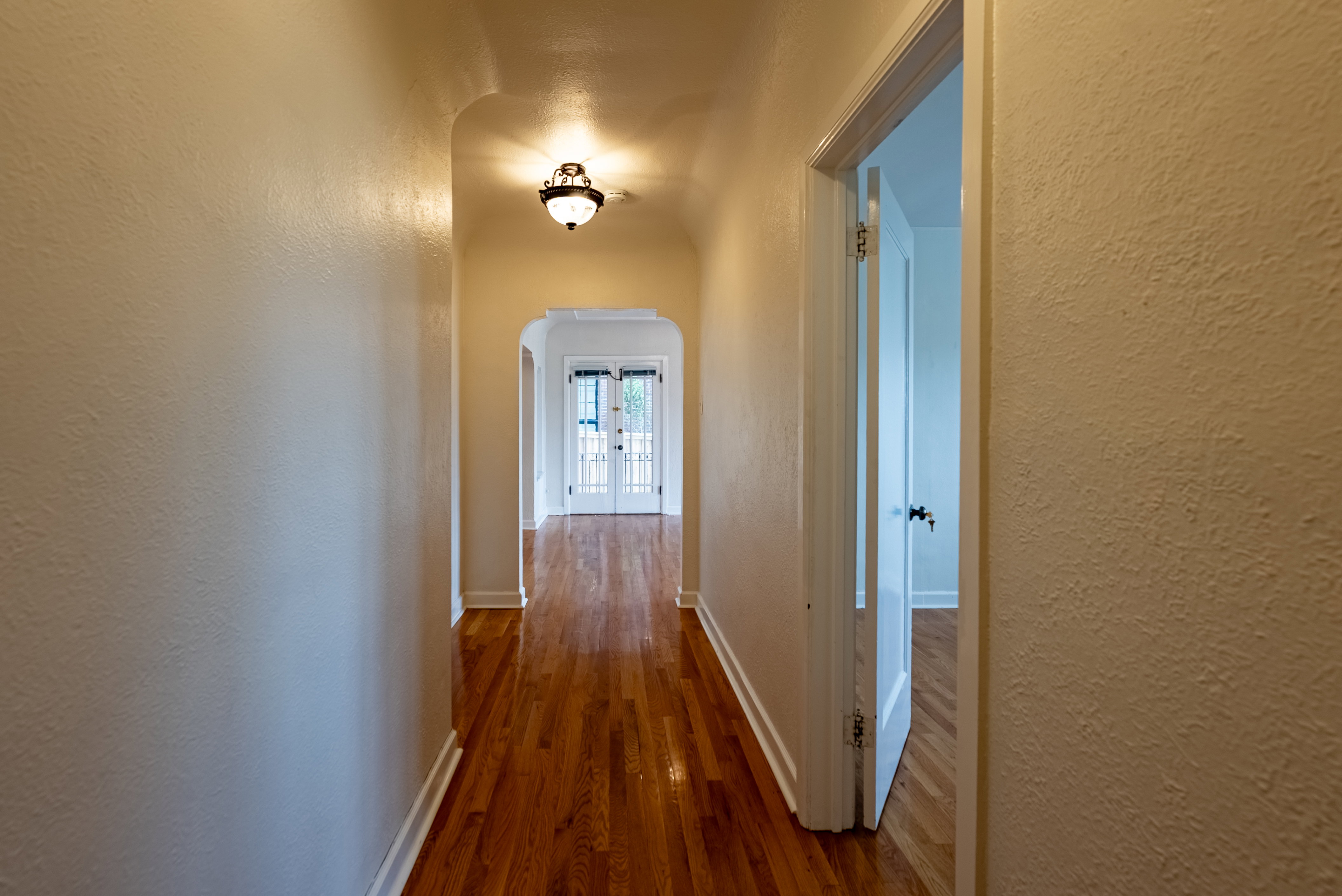Hallway featuring hardwood flooring, an arched entryway, and a decorative flush-mount light fixture