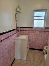 Apt # 9 > Half bathroom with a wainscoted wall, vanity, tile walls, and light tile patterned floors