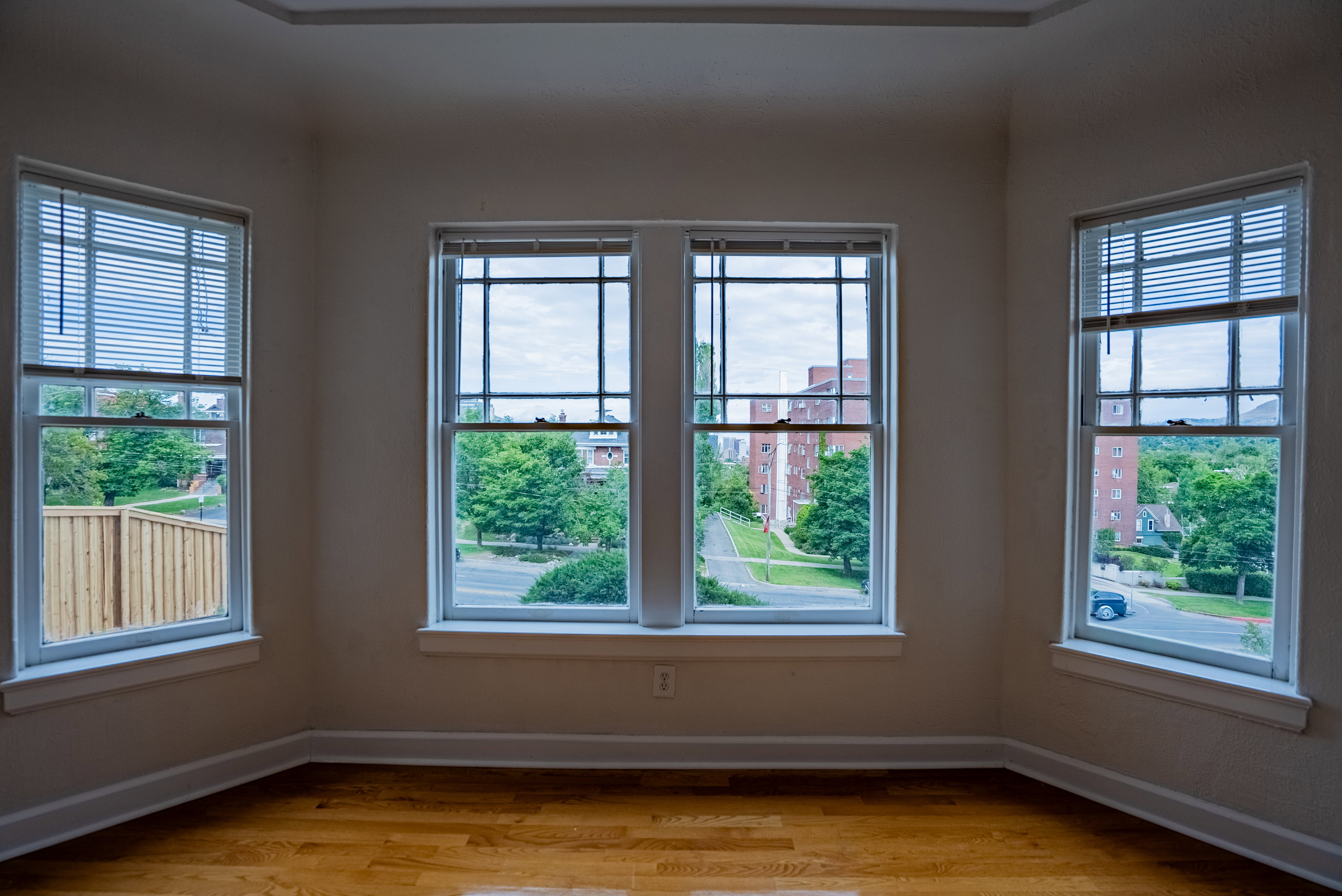 Bright interior room featuring a bay window formation with four individual windows, each equipped with white blinds