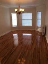 Apt # 7 > Unfurnished room featuring dark wood-style flooring, radiator, and a chandelier