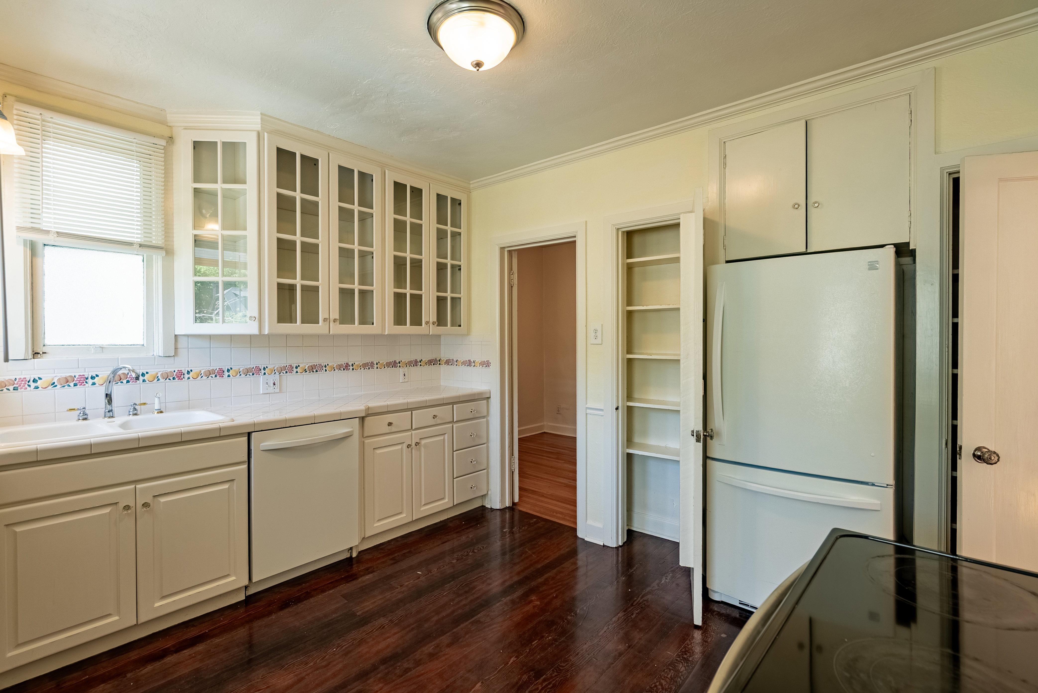 Kitchen featuring white cabinetry with glass-front uppers, a dual-basin sink, and wood-finish flooring