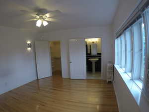 Apt #2 > Unfurnished bedroom featuring a walk in closet, light wood finished floors, radiator heating unit, a ceiling fan, and connected bathroom