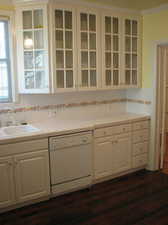 Apt # 11 > Kitchen featuring white cabinets, light countertops, dishwasher, glass insert cabinets, and dark wood-type flooring