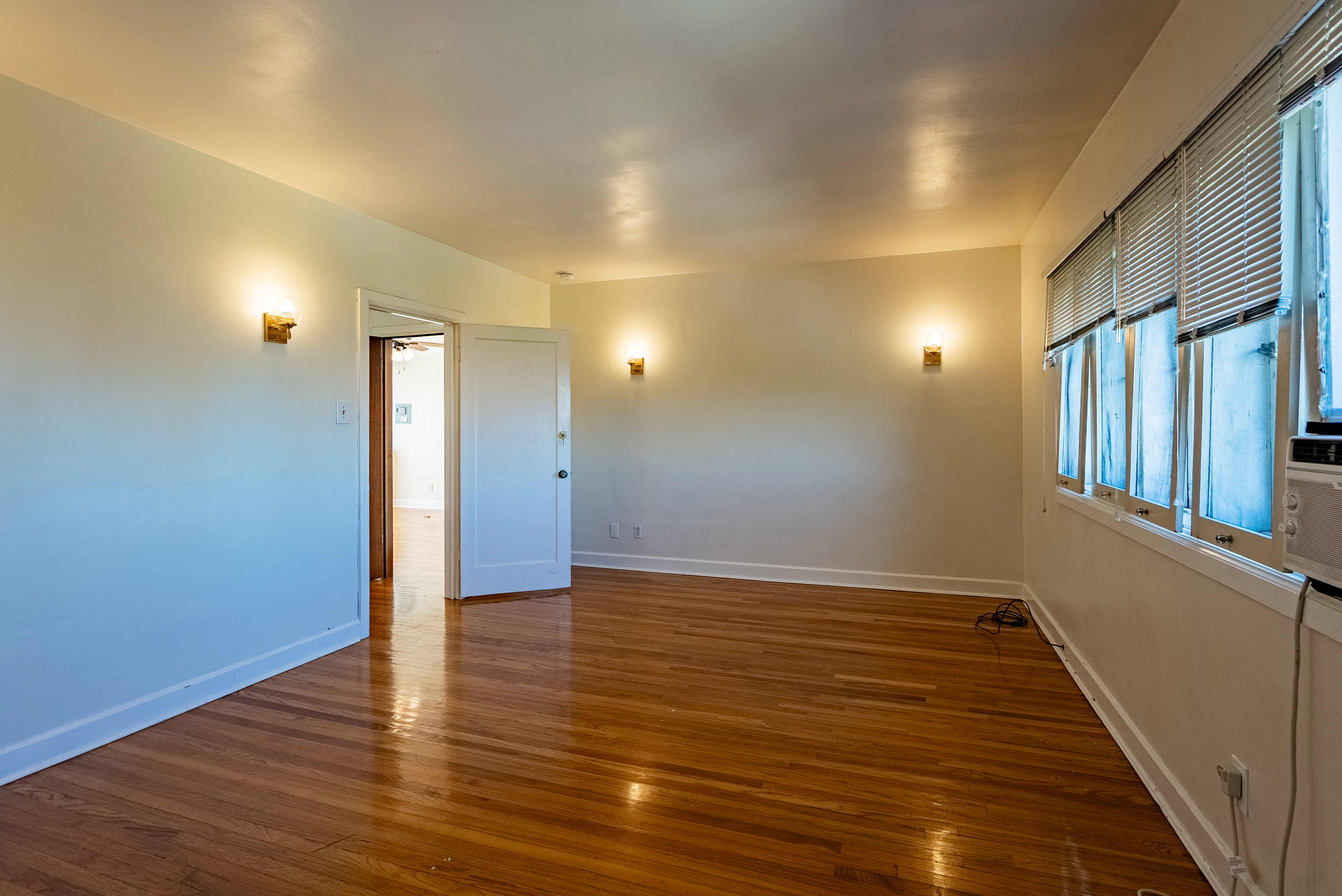 Hardwood flooring in a room with white walls, multiple windows, and wall sconces