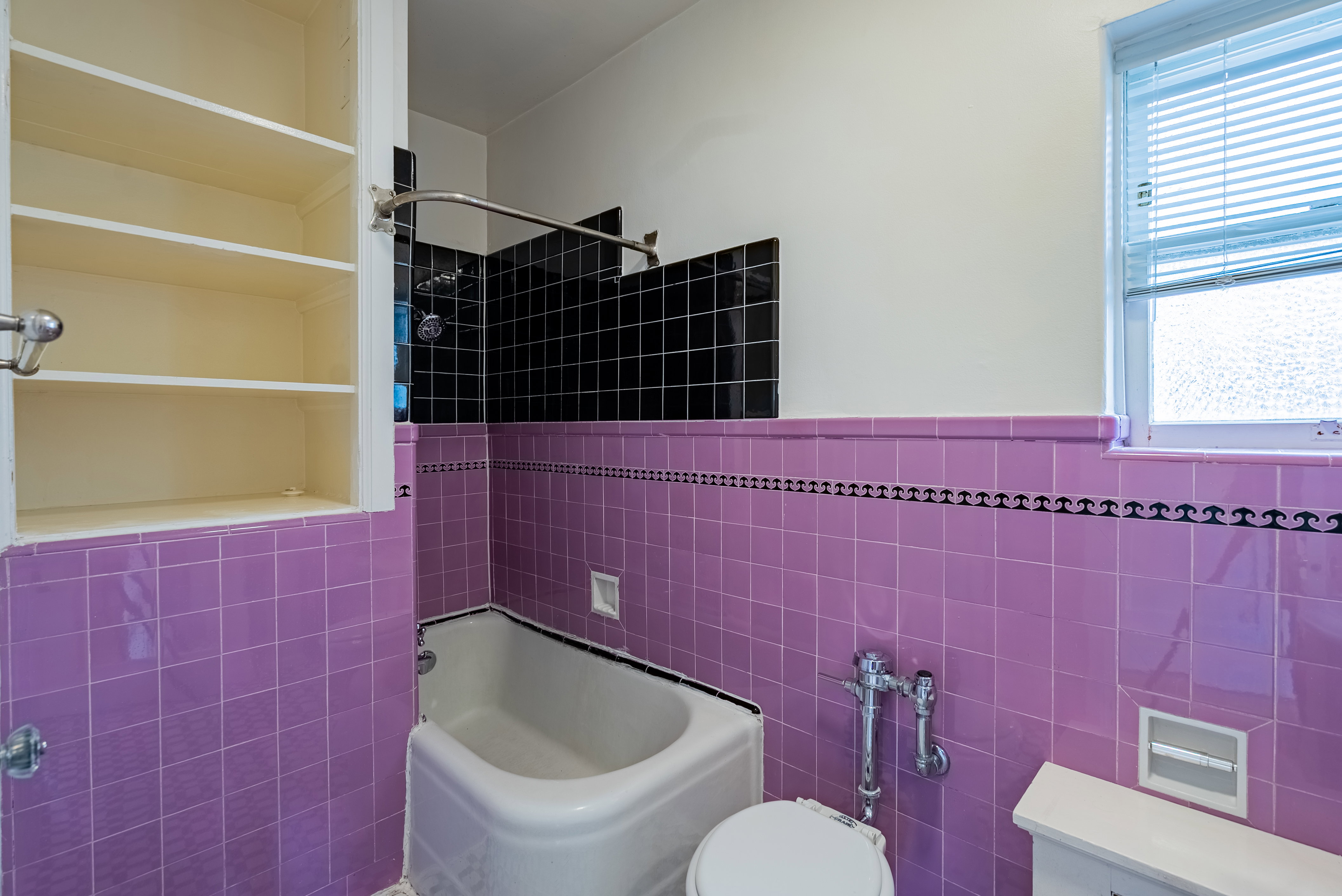 Bathroom featuring a bathtub, purple and black tilework, and a built-in wall cabinet with shelving