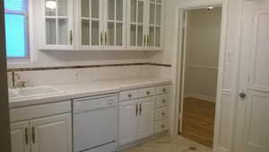 Apt # 7 > Bar area with tile countertops, white cabinetry, dishwasher, and glass insert cabinets