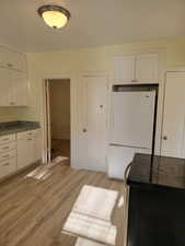 Apt # 9 >  Kitchen with white cabinetry, black electric range, freestanding refrigerator, light wood-style floors, and dark stone counters